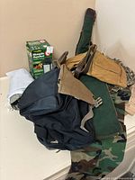 Photo of outdoor gear including camouflage pants, various ponchos, sports bags, and mosquito repellent lantern.