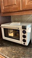 White Tovala countertop smart oven with manuals on top, placed on granite countertop under wooden kitchen cabinets.