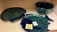 Green pottery ocean set including round bowl with fish scale texture, fish-shaped platter, and shell-shaped platter, all glazed in green-blue shades.