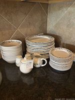 Overview of entire stoneware set including stacked plates, bowls, and condiment set on a countertop.