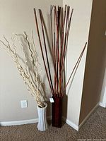 Two decorative vases, one white ceramic with curly branches, one dark wood tall rectangular vase with long thin branches.