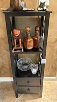 Front view of the black wooden shelf showing two levels of shelving and two drawers with metal pulls. Various decorative items are placed on shelves but not included in sale.