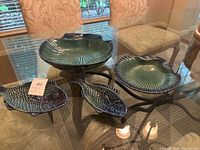 Photo showing all three pieces in the set on a glass table: two fish-shaped dishes and one shell-shaped dish elevated on black stands.