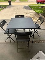 Full view of square black table with four black folding chairs around it.