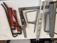Photo of pipe wrenches, handsaw, level and square on white table