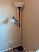Full view of the torchiere floor lamp showing black base, tall black pole, large white torchiere shade on top, and smaller adjustable reading light extension with white shade.