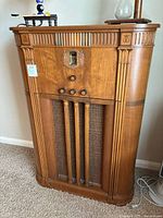 Full front view of vintage wooden radio cabinet showing decorative carving, control knobs, and speaker grille.