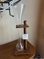 Full view of the vintage glass ale sprinkler mounted on wooden stand, showing the long neck and bulbous base of clear glass.