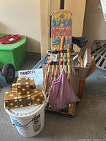 Photo shows a bucket with the stacked large wooden Yardzee dice, croquet set mallets and balls behind, and partially visible box of board games Clue, Aggravation, and Stratego, as well as handheld Bagatelle game.