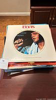 Stacked vinyl albums with Elvis Presley album on top showing photographic cover with singer in performance.