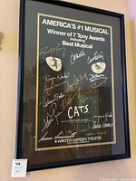 Framed Cats musical poster signed by multiple cast members, hanging on wall, showing full view of frame and signatures.