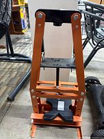 Front view of the orange steel hydraulic shop press showing the full frame and black X-shaped base plate at the bottom, without the hydraulic pump or lever attached.