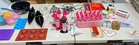 Wide view of the assortment of baking accessories including molds, baking cups, cookie cutters, and kitchen tools arranged on a table.