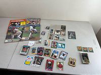 Wide shot showing assortment of baseball cards arranged on a table, along with four sports magazines in the background.