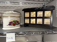 Photo of Knotts Berry Farm ceramic canister with fruit design next to wooden spice rack with eight labeled porcelain drawers.