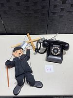 Charlie Chaplin marionette puppet lying on table next to rotary style push button phone