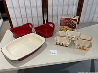 Photo showing all included items: Rachel Ray red ovenware dishes, Paula Deen casserole, small decorative loaf dishes, and the boxed Crème Brûlée set.