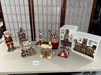 Multiple Dickens Village and Christmas figurines arranged on a table including Santa Claus, Gingerbread House, Snowman, Reindeer, and other festive decorations.