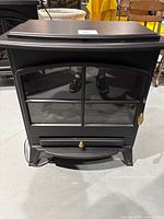 Front view of the black composite wood and plastic electric heater resembling a wood stove with a divided glass window and brass knob.