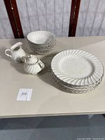 Photo of the entire set including 6 dinner plates stacked, 8 bowls stacked, a creamer, and a sugar bowl with lid, all white with silver edging and swirl pattern.