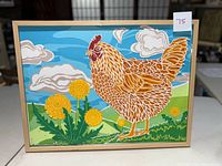 Full view of the framed paper artwork of a hen surrounded by yellow flowers and green grass under a blue sky with clouds.
