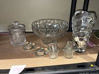 Image showing a large glass bowl with floral design, a molded vase, a glass dish with lid, and the heart-shaped votive holders arranged on a shelf.