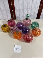 Full view of 10 assorted colorful glass fruit-shaped bud vases and one small purple plastic pumpkin on table