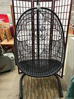 Front view of black plastic wicker hanging egg chair on metal stand.