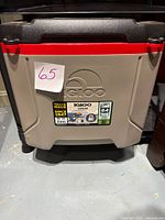 Front view of the cooler showing the gray body, black hinged lid with red rim, labeled with capacity and Texas made stickers.