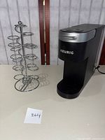 Photo showing Keurig K900 coffee machine and metal spinning pod holder side by side on a white surface.
