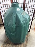 Grill covered by green vinyl protective cover showing embroidered Big Green Egg logo