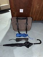 Messenger bag and three folded umbrellas placed in front of wooden background.