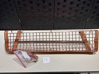 Front view of copper colored metal kitchen rack with mesh grid and packaging with hooks.