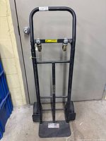 Front view of Milwaukee black steel hand truck in upright position, showing handle, wheels, and base plate.