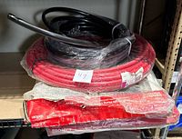 Photo showing red PEX tubing coil, black tubing, and two wrapped utility windows on a shelf.