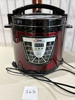 Front view of the Power Pressure Cooker XL showing its red metallic body, black top with handle, and digital control panel with buttons and LED display.
