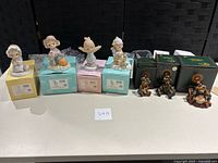 Seven figurines on display with their respective boxes, four Precious Moments on pastel boxes and three Boyd's Bears with green boxes.