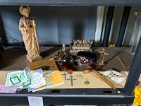 Display shelf with beige plastic statue of Saint Jude, resin Last Supper sculpture, various crosses, prayer book, and miscellaneous small religious items.