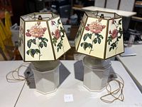 Pair of table lamps, each with a hexagonal floral canvas shade and white ceramic octagonal base, positioned side by side on table.