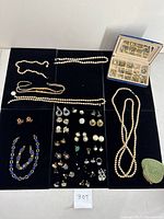Overview of the lot showing five strands of pearl necklaces laid out with a jewelry box of assorted earrings and a blue gold-beaded purse.