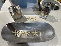 Photo showing the silver colored oval bowl with four small starfish and two decorative lantern pieces on a table.