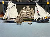 Front view of five model sailboats including a multi-sail Gorge Fock, a small Santa Maria, two half ship wall mounts, and a small fishing boat for scale.