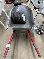 Full view of the wheelbarrow with the four spare tires inside the tub, showing the metal frame with red handles and grey tub.