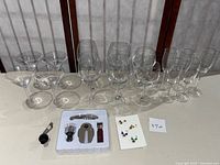 Full assortment of wine glasses, champagne flutes, wine opener set, and wine glass charms arranged on table.