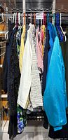 Photo of assorted women's clothing hanging on a rack, includes various tops, dresses, and skirts, many with tags, mostly petite size.