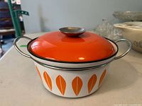 Pot with orange lid on, showing lotus leaf pattern around white pot and metal handles.