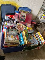 Four large bins filled with children’s books, including Dr. Seuss’s Cat in the Hat, fairy tales, Scholastics, and other titles. Also includes miscellaneous items such as pencils, masks, stickers, and CDs.