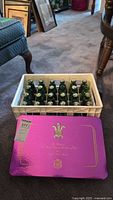 Full view of 20 green collectible Canada Dry bottles in a white plastic crate with the purple commemorative box lid in front.