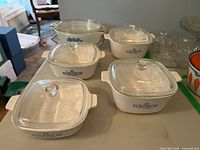Photo of five casserole dishes: four Corningware Blue Cornflower pattern in various sizes, one additional clear glass dish by Anchor Hocking-Fire King with a lid showing small chip.