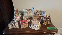 Photo of nine assorted cottage and castle figurines displayed on a wooden surface. One notable castle is centrally placed with smaller cottages arranged around it.